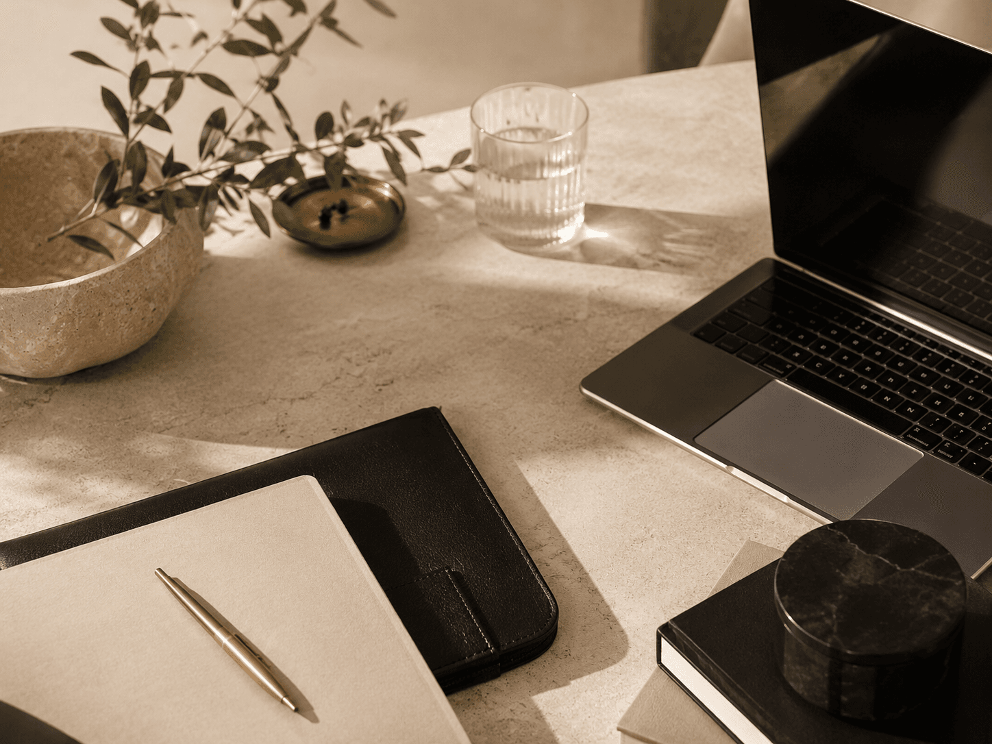 An orderly desk with a laptop, a notebook and a pen